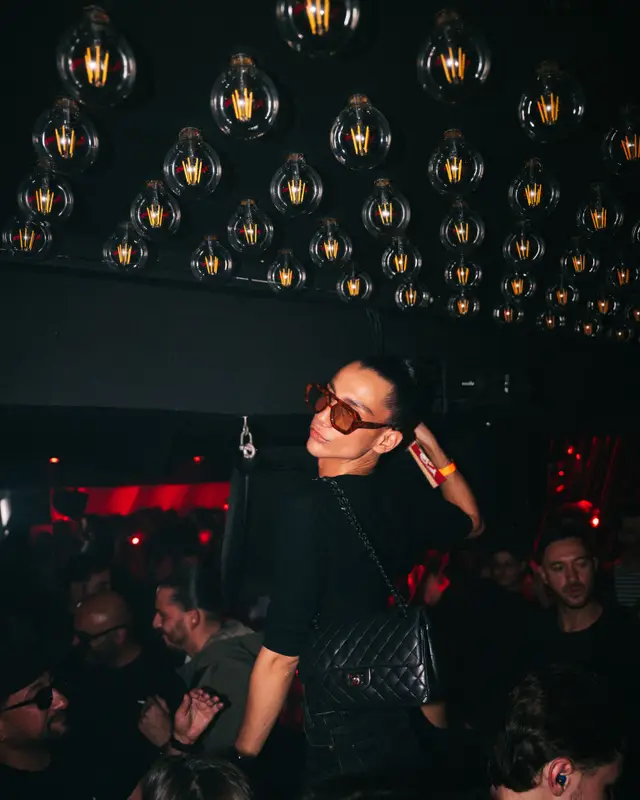 Une jeune femme en lunettes noires danse sous un plafond d’ampoules, au-dessus de la foule du Barta
