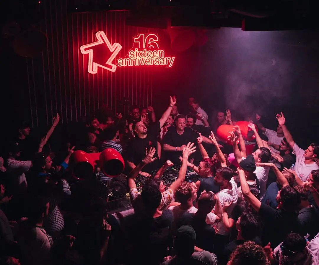 La foule bras levés devant le néon rouge « 16 sixteen anniversary » du Baby Club