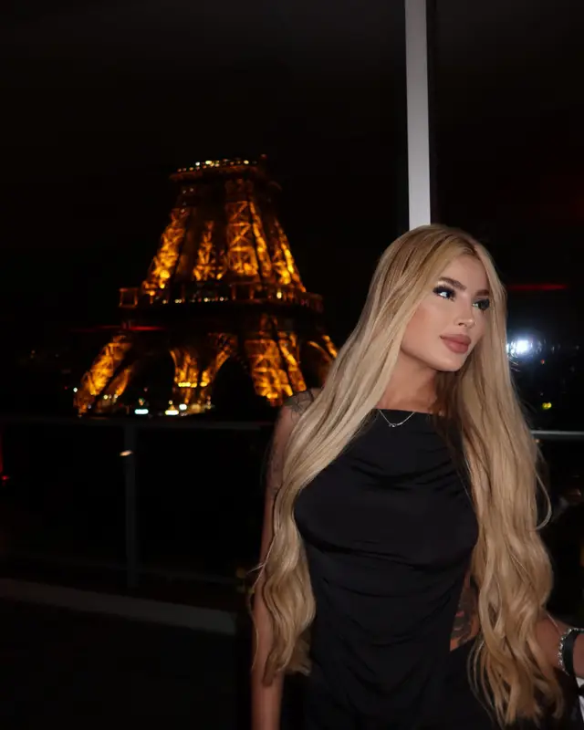 Une femme en robe noire pose sur le rooftop du 10ème Ciel, la tour Eiffel illuminée derrière elle