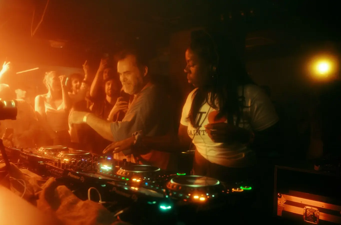 Deux DJ penchés sur les platines du Rex Club, dans une lumière orangée, la foule tout près