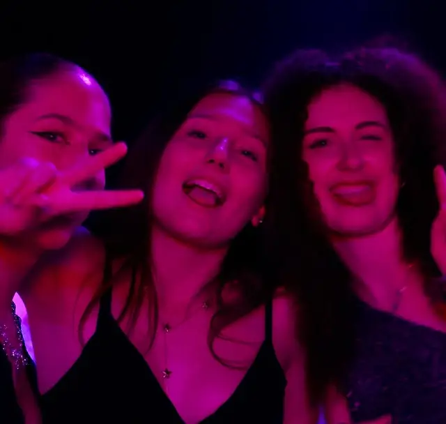 Trois amies serrées face à l'objectif, sous les néons de la Maison M.