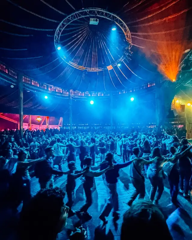 Une foule danse sous le chapiteau du Cabaret Sauvage, éclairée de bleu, autour de la structure circulaire du plafond